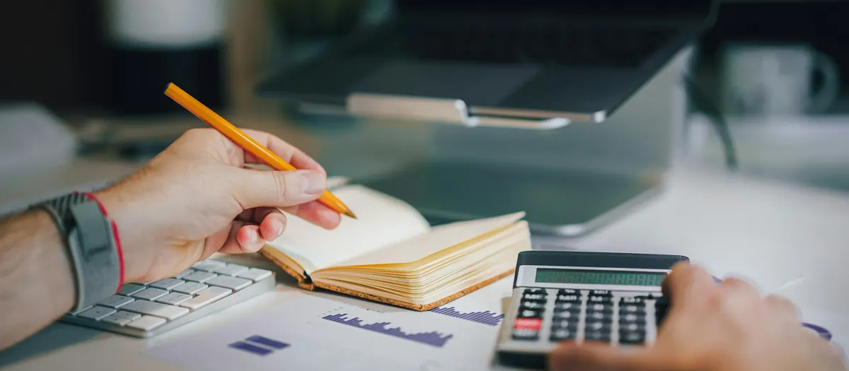 Hands using a calculator and notebook at a desk